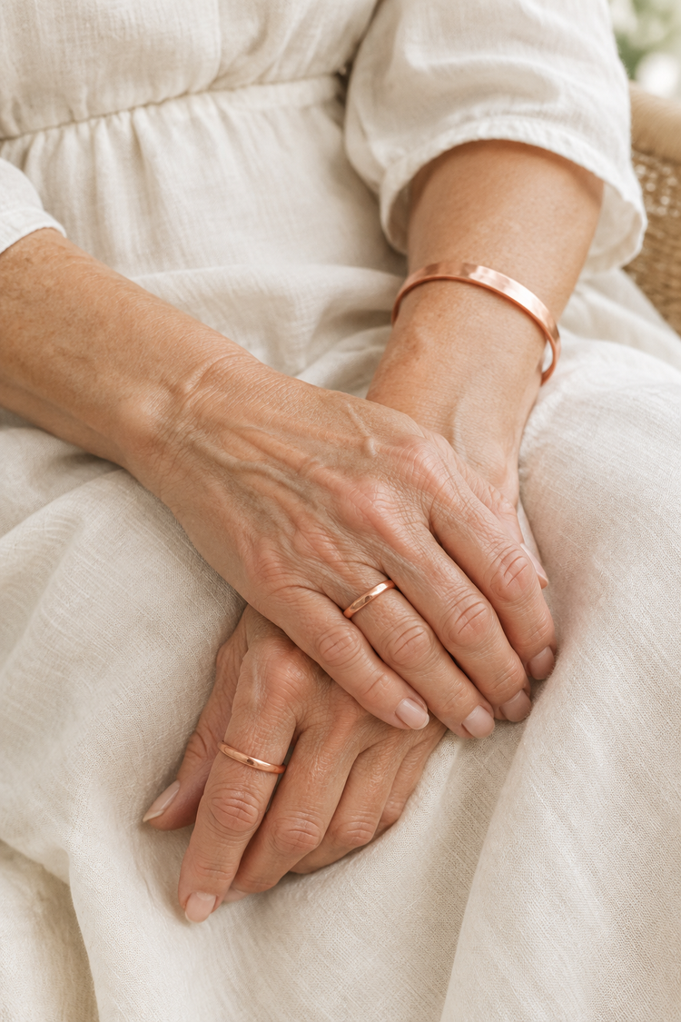 Hands wearing copper rings and a copper cuff resting on linen