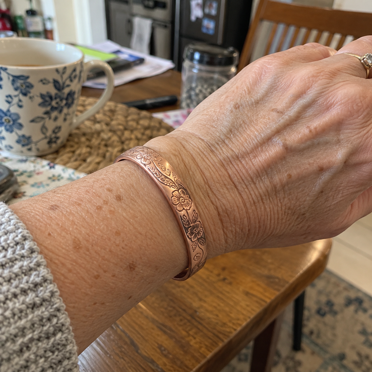 Close-up of a wrist wearing an engraved floral copper cuff bracelet at a kitchen table