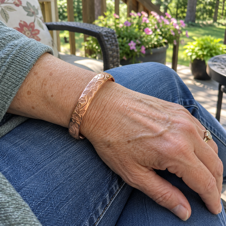 Wrist wearing an engraved floral copper cuff bracelet, relaxing outdoors on a sunny patio