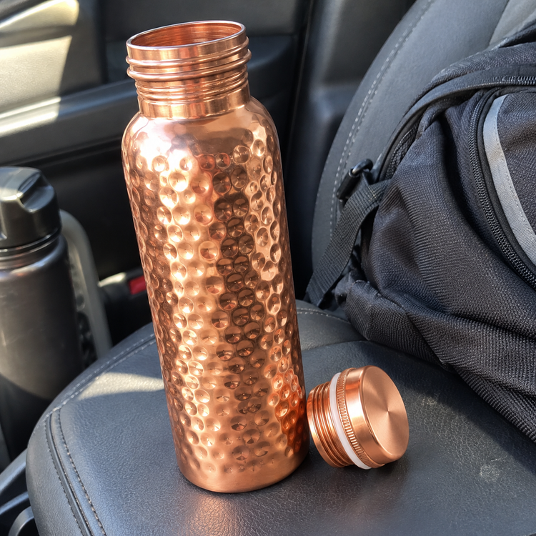 Hammered copper water bottle with its lid off on a car seat